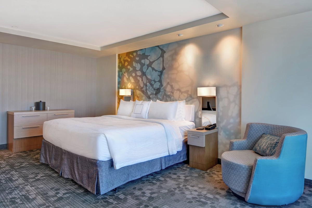 A hotel room with a large bed, a chair, a nightstand, and a wall with a textured mural.