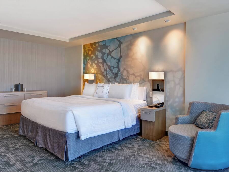 A hotel room with a large bed, a chair, a nightstand, and a wall with a textured mural.