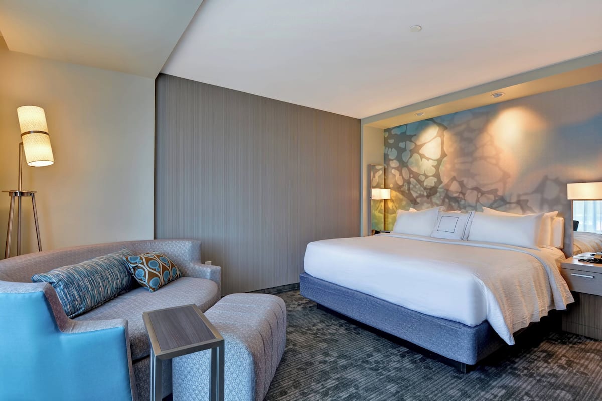 A hotel room with a bed, a sofa, a small table, and a wall with a decorative mural.