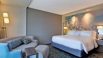 A hotel room with a bed, a sofa, a small table, and a wall with a decorative mural.