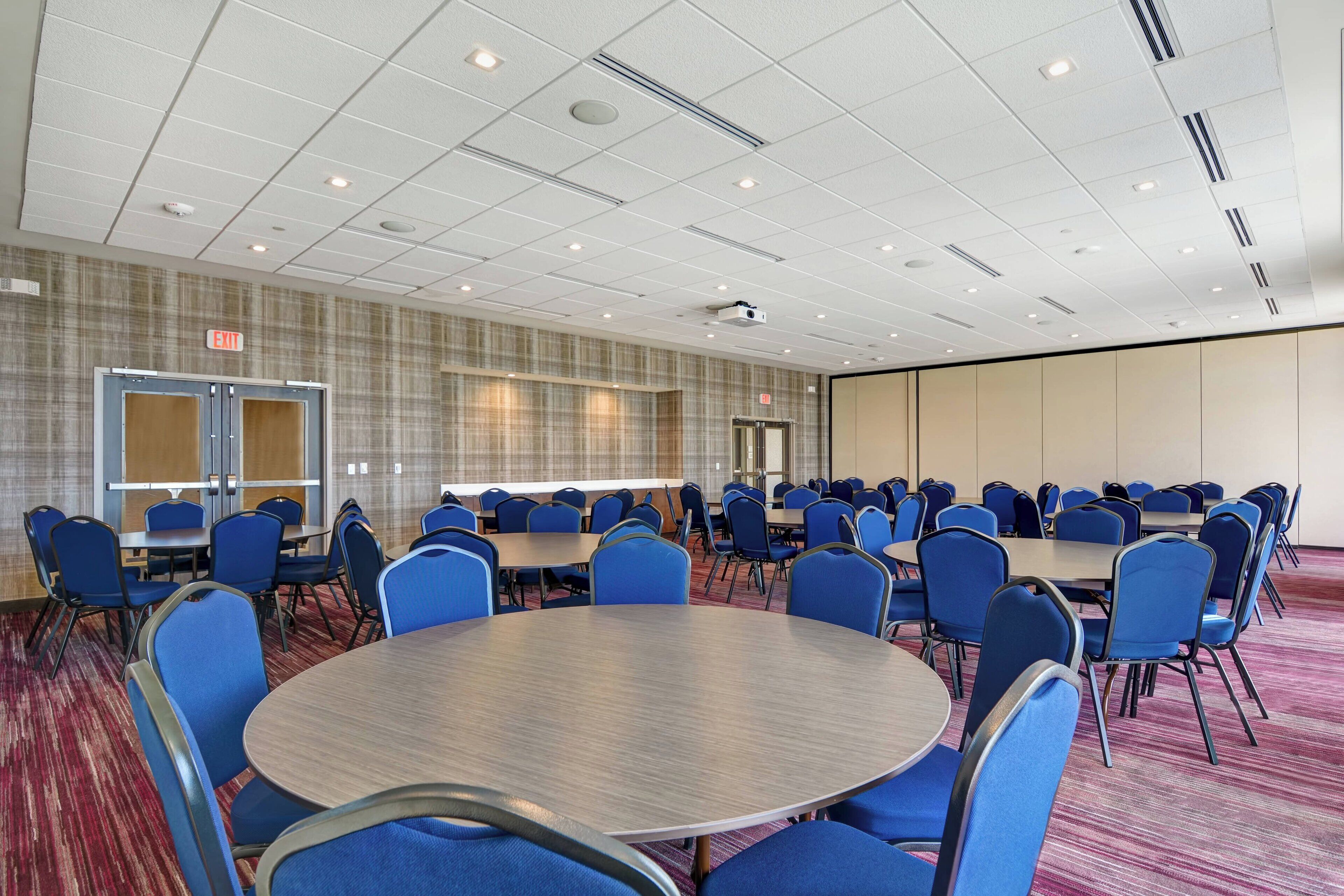 Une salle de conférence avec des tables rondes et des chaises bleues, un sol recouvert de moquette et un mur orné de motifs.
