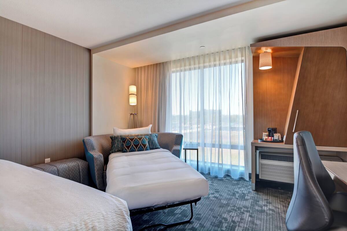Une chambre d’hôtel avec un lit, un bureau, une chaise et une vue sur l’extérieur.