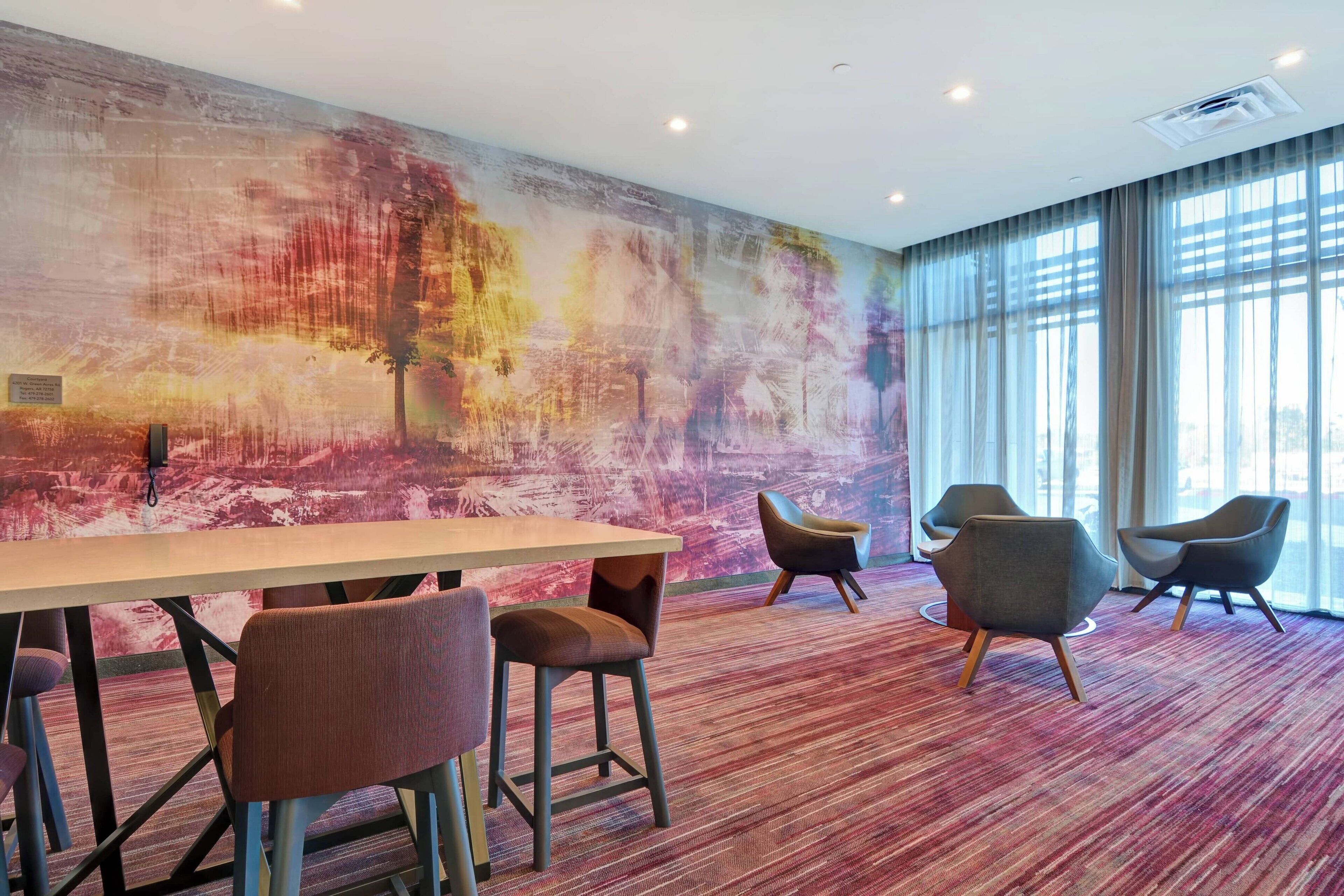 A conference room with a long table and four chairs, a large abstract mural on the wall, and large windows with curtains.
