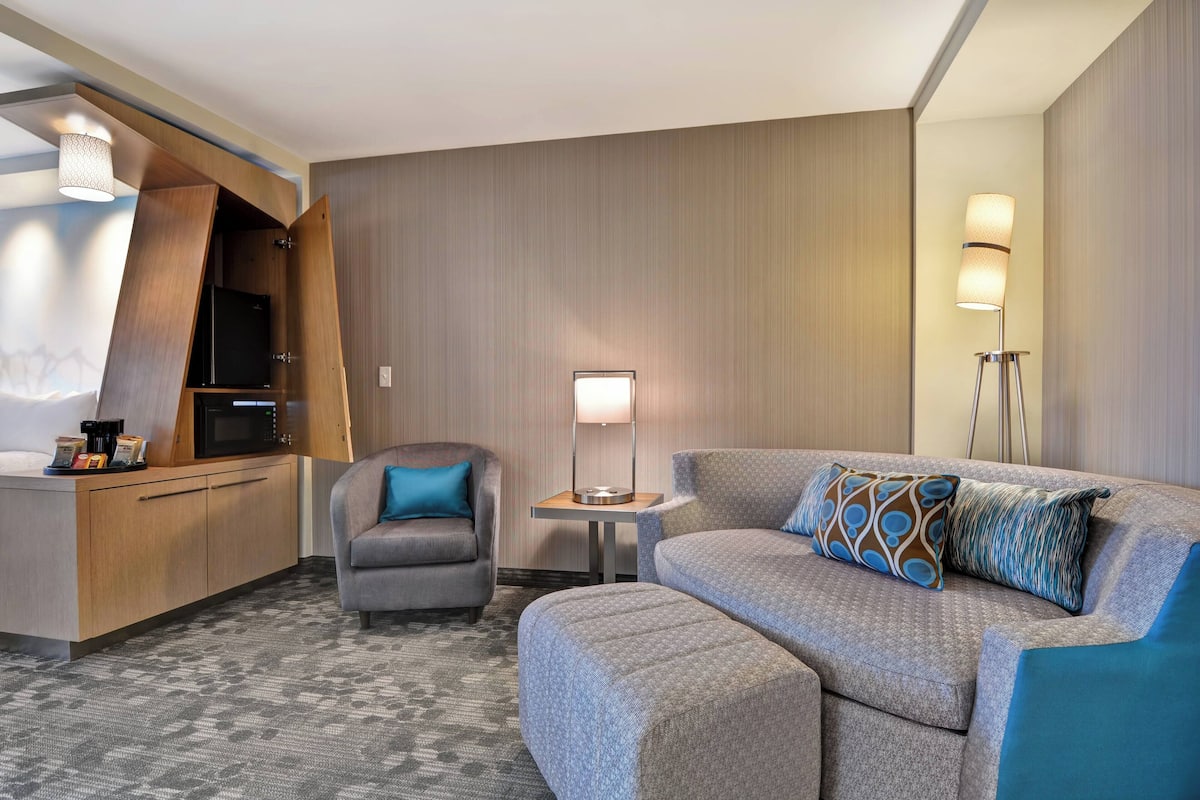 Une chambre d’hôtel moderne, équipée d’un canapé, d’un fauteuil et d’une petite table avec une lampe.