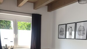 A modern living room with a dark sofa, geometric patterned pillows, a round side table, and a grey furry rug. There are three framed geometric wall art pieces above the sofa.
