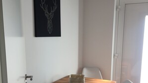 A dining area with a wooden table and two white chairs, a black wall art of a deer, and a white door.