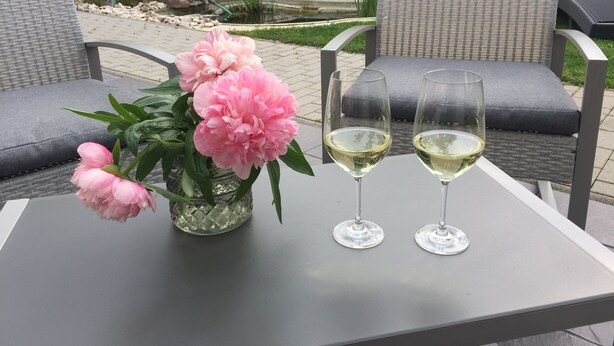 A patio with wicker chairs, a table with two wine glasses, and a vase with pink flowers.