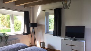 A bedroom with a bed, a TV on a white dresser, a standing lamp, and a window with curtains.
