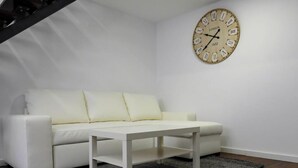 En moderne stue med en hvid sofa, et lille hvidt bord og et rundt vægur.