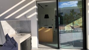 Une cuisine moderne dotée d’un évier encastré et offrant une vue sur un patio grâce à une porte vitrée.
