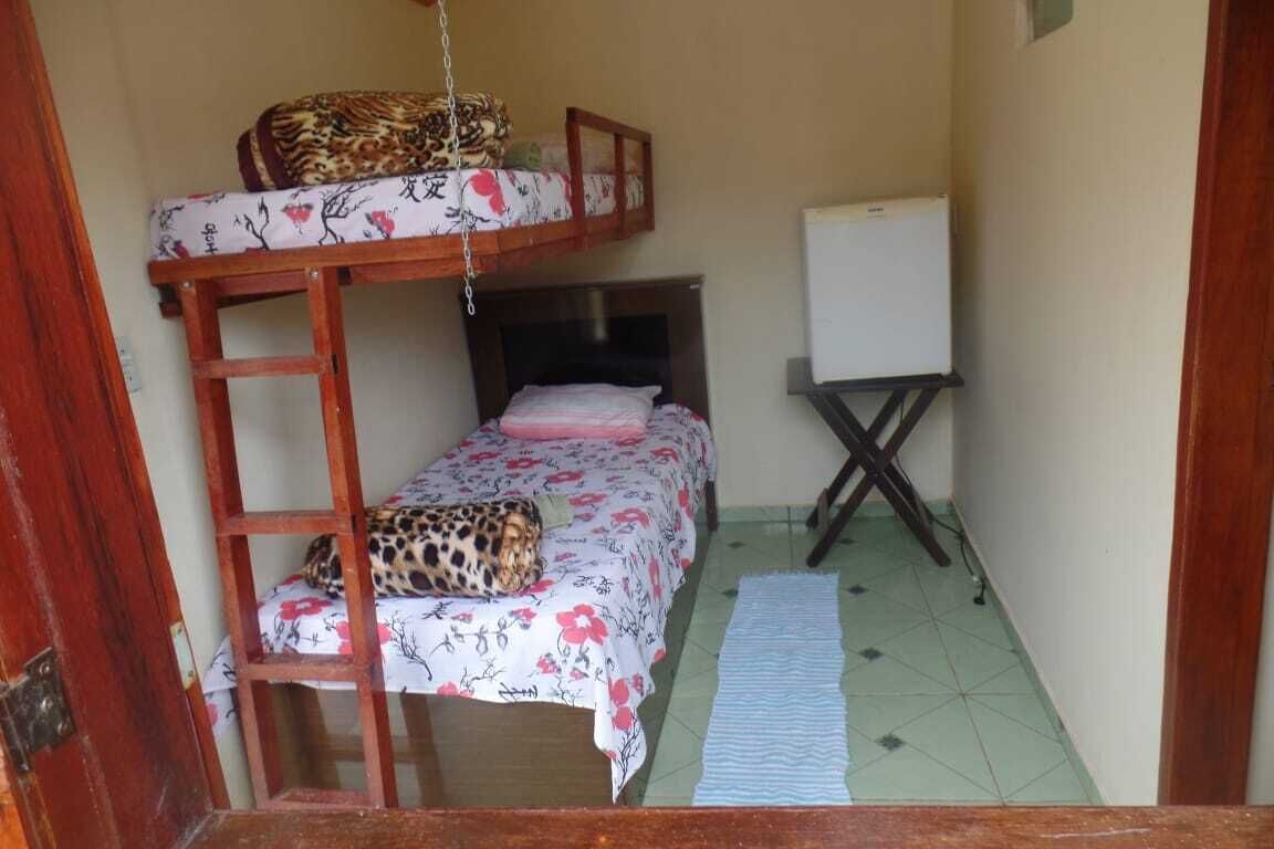 Quarto pequeno e compacto com beliche, uma cama de solteiro, quadro branco e mesa pequena.