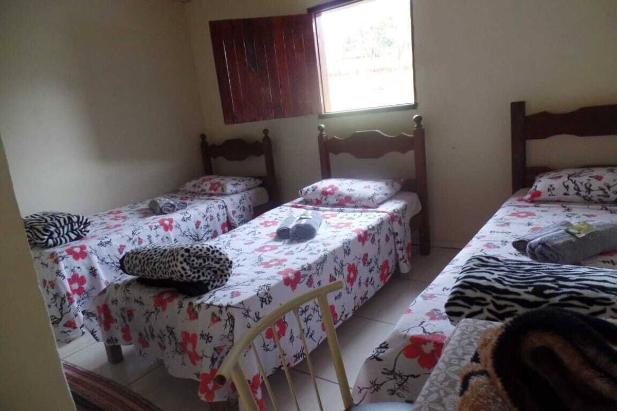A room with two single beds, each with a floral bedspread and a leopard print pillow. There is a window with wooden shutters, and the room has a tiled floor.