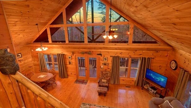 Ein Holzblockhaus im Inneren mit Essbereich, einer Couch, einem Fernseher und einer Treppe.