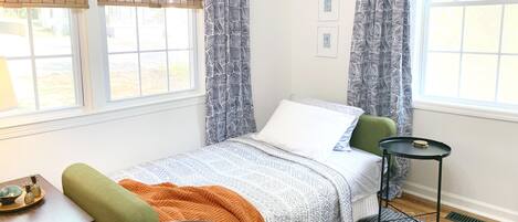 Une chambre à coucher avec un lit, une chaise, une table et une fenêtre avec des rideaux.
