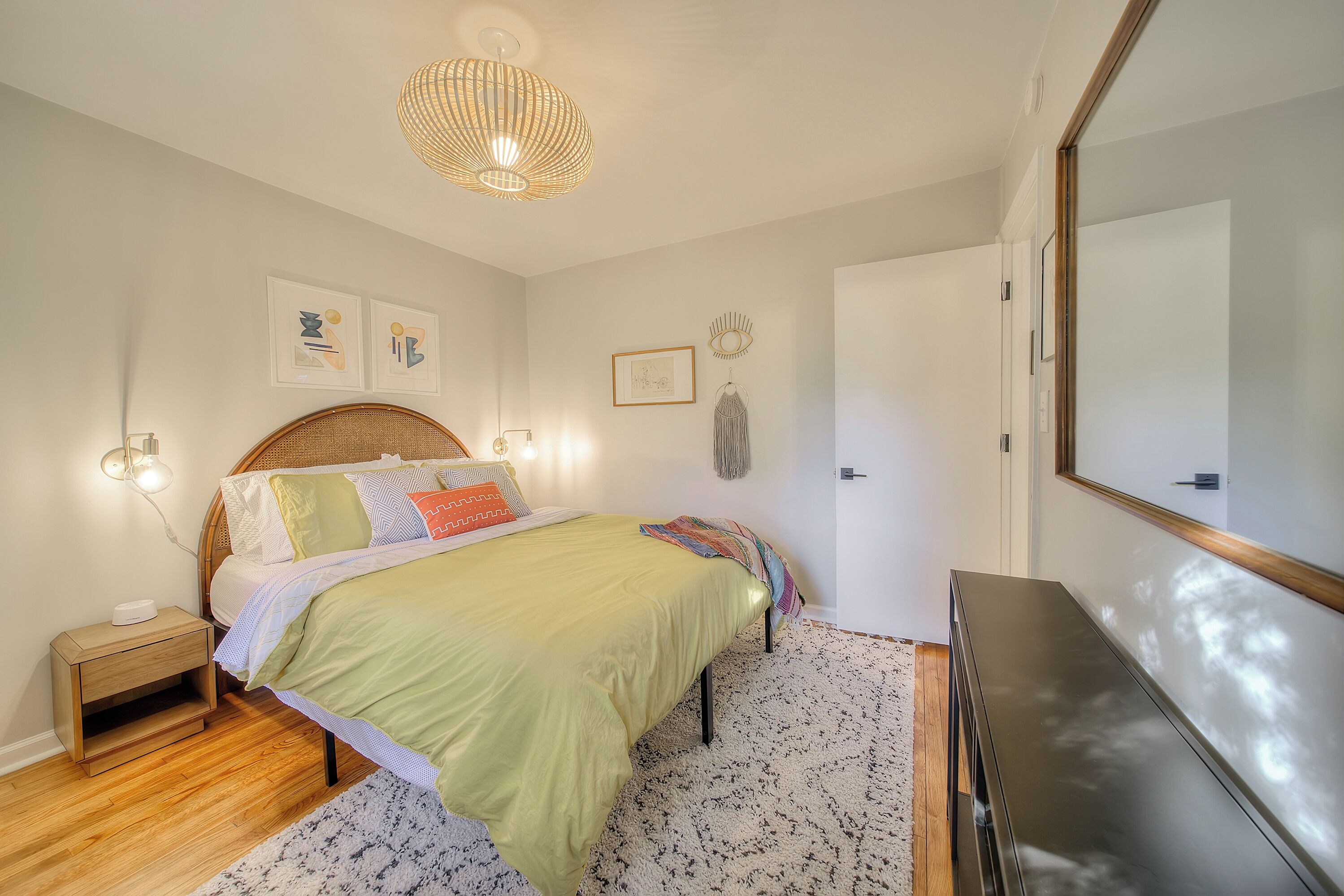 Een slaapkamer met een bed, nachtkastje, lamp en een spiegel aan de muur.