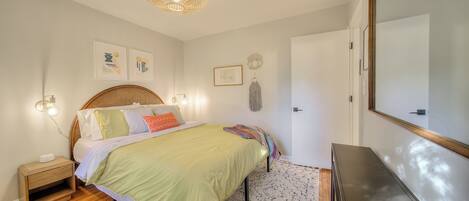 Een slaapkamer met een bed, nachtkastje, lamp en een spiegel aan de muur.