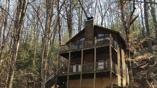 A wooden cabin with a balcony, surrounded by trees.