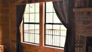 A wooden cabin room with a bed, a fireplace, and large windows with curtains.