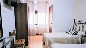 A hotel room with two beds, a desk, a chair, and a window with curtains. - Pensión Cuadrado (Seron)