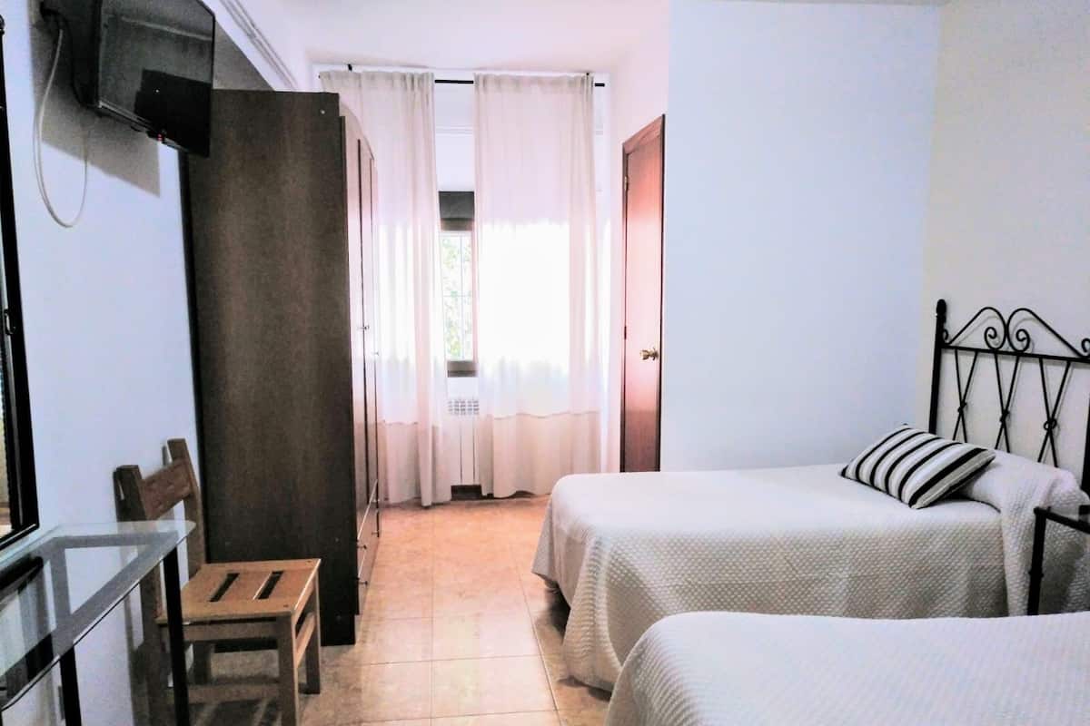 A hotel room with two beds, a desk, a chair, and a window with curtains.