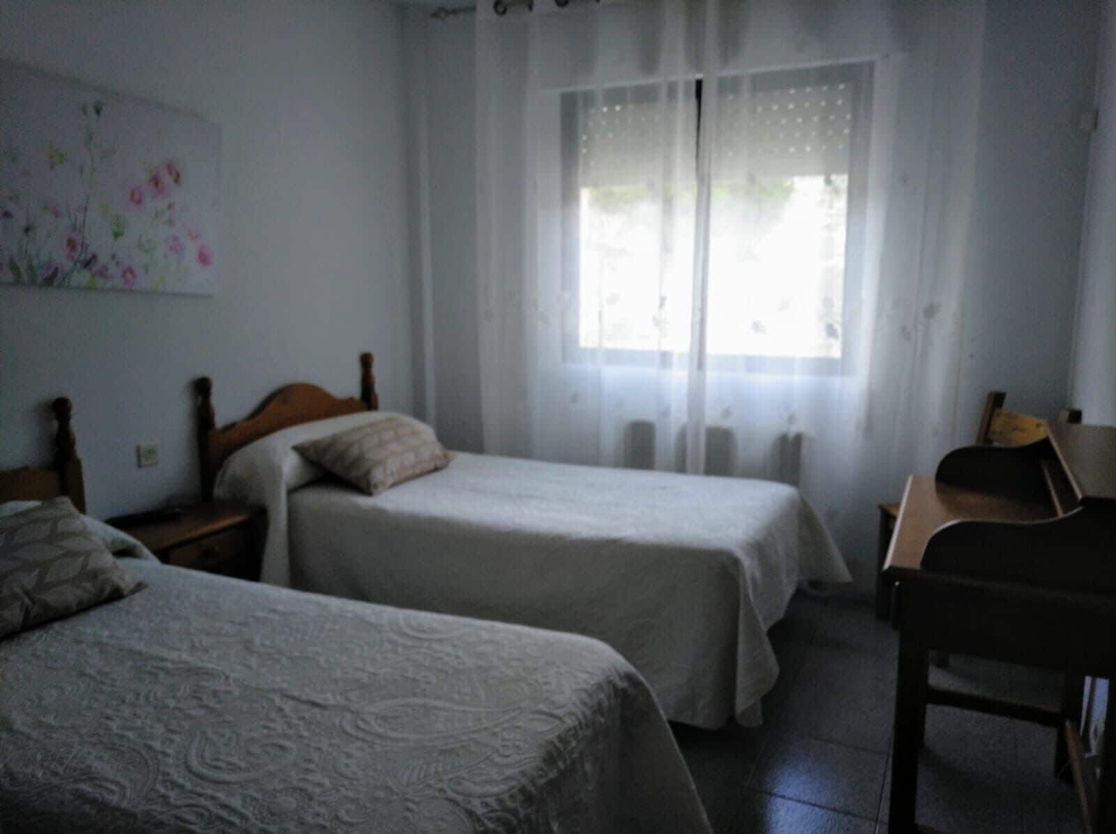 A room with two single beds, a desk, and a chair.