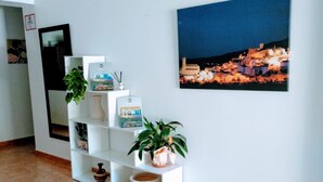 A hallway with a white shelving unit displaying various decorative items and a framed photograph of a coastal town at night. - Pensión Cuadrado (Seron)