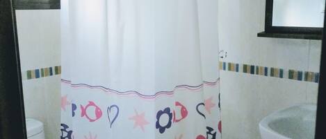 A bathroom with a white shower curtain featuring a pattern of hearts, stars, and fish. There is a white toilet and a sink with a mirror above it.