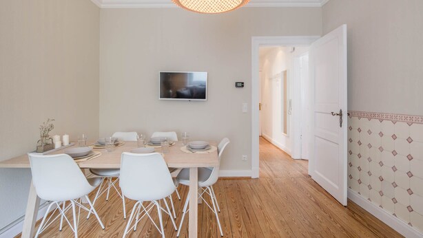 A dining area with a wooden table, white chairs, a television, and a patterned wall.