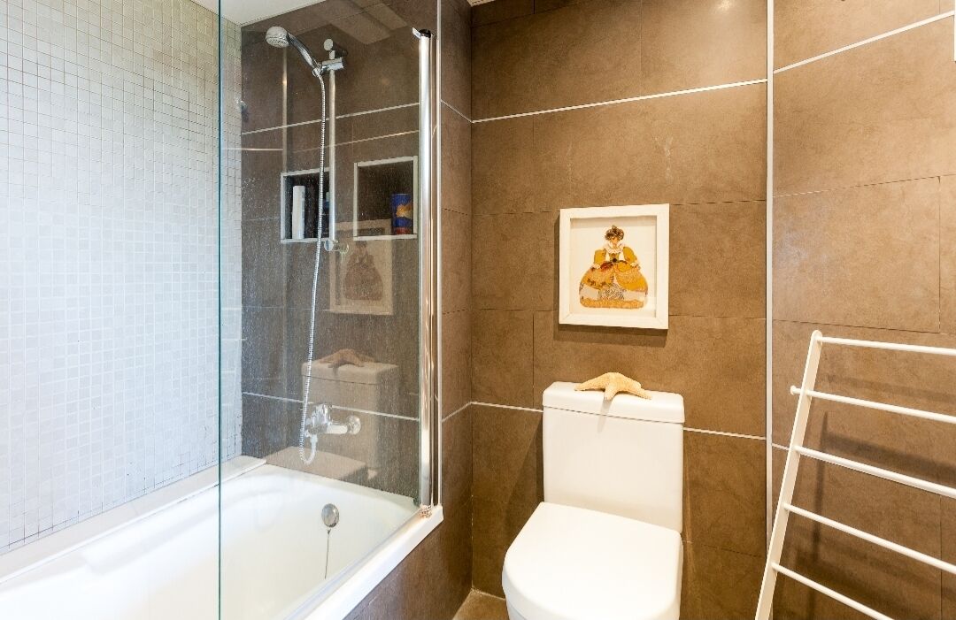 A bathroom with a glass-enclosed shower, a white toilet, and a framed picture on the wall.