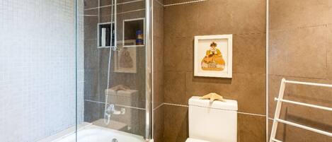 A bathroom with a glass-enclosed shower, a white toilet, and a framed picture on the wall.