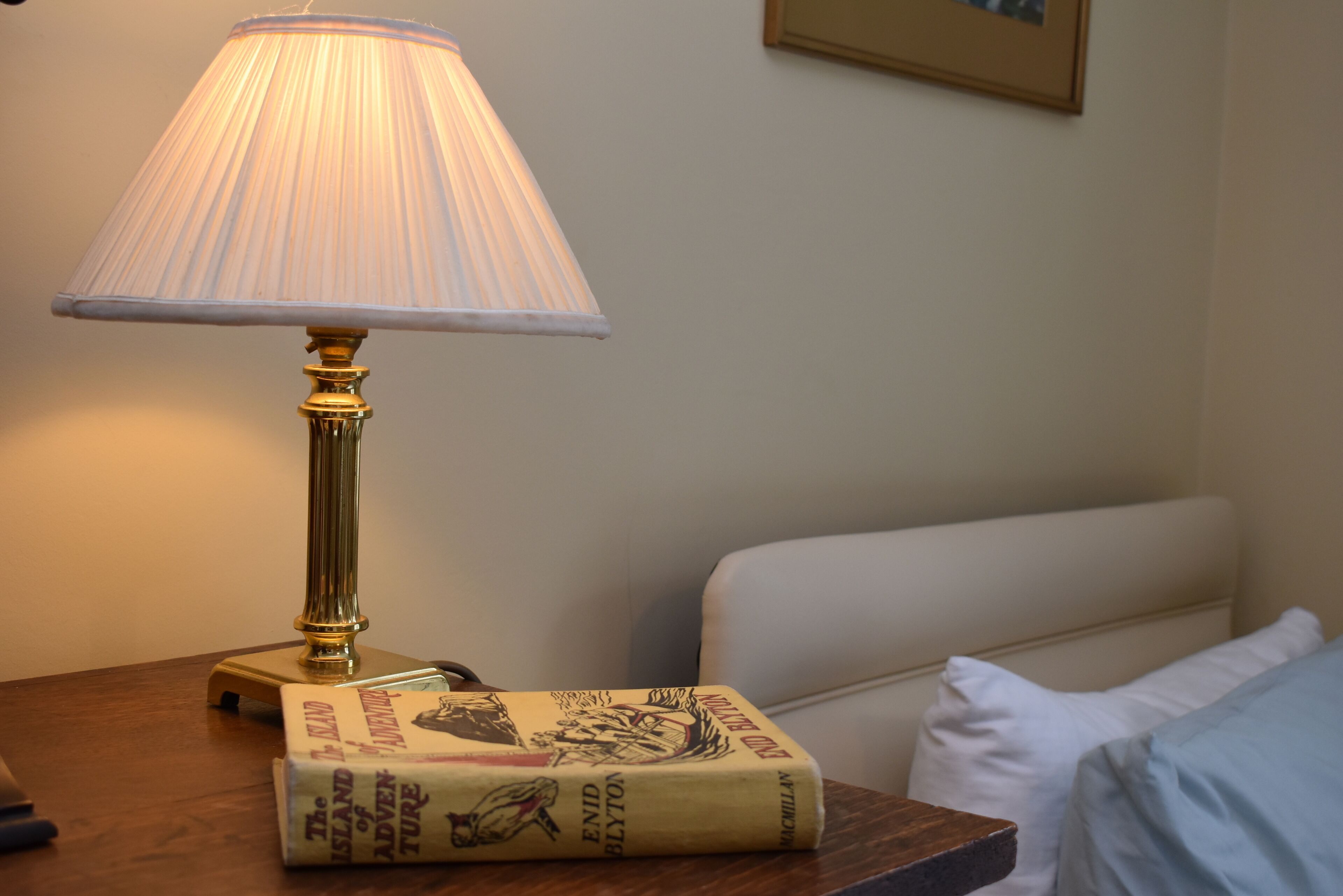 Une lampe posée sur une table en bois, à côté d’un lit agrémenté d’oreillers blancs.
