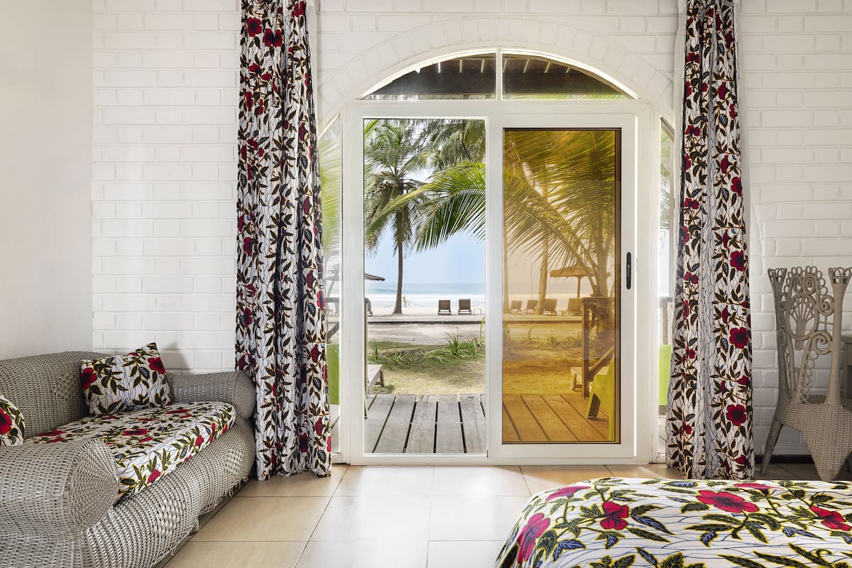 A beach view through a glass door, a wicker sofa, and a bed with floral bedding.