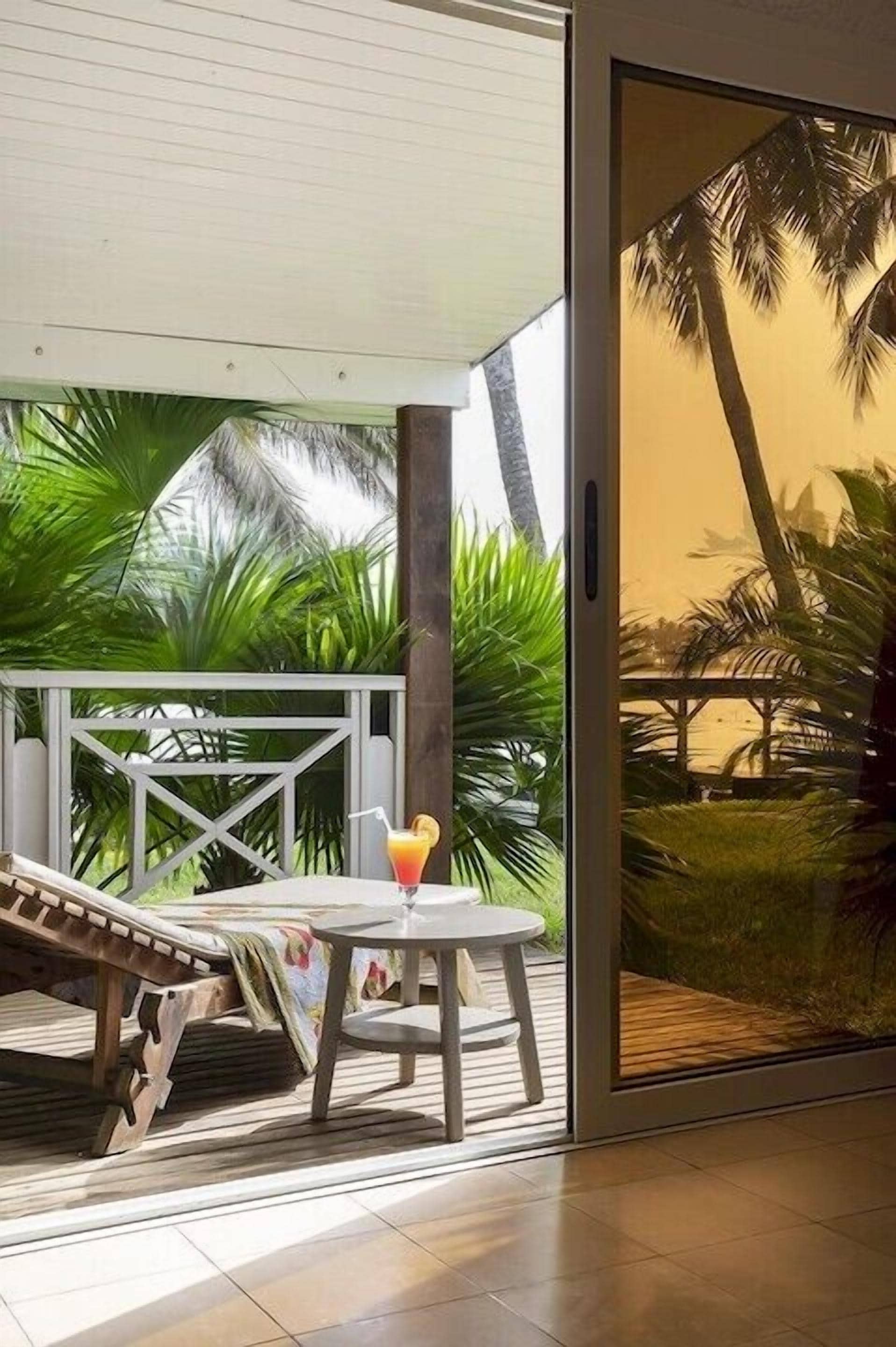 Une chaise longue et une table avec une boisson sur un balcon offrant une vue sur les palmiers.