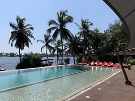 Piscina cristalina con sillas de reposo rojas y palmeras, con vista a una extensión de agua.