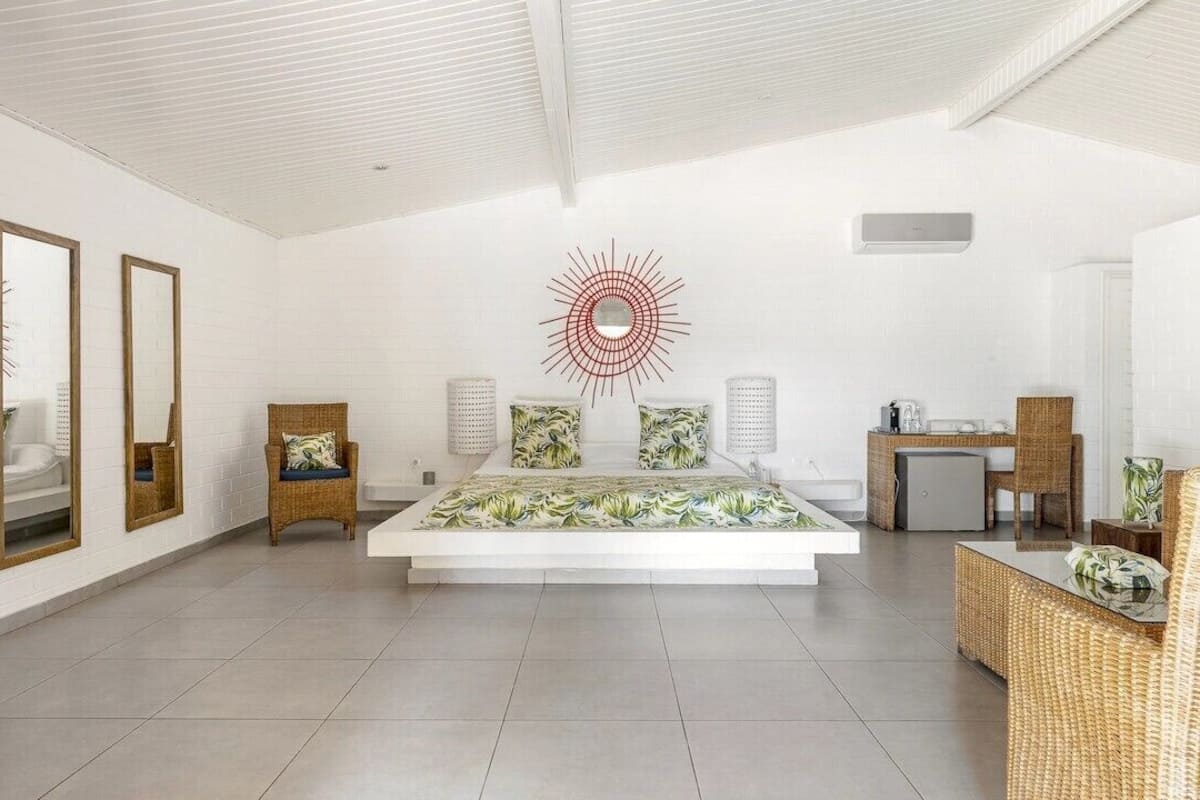 A spacious bedroom with a large bed, a wall-mounted red abstract art piece, and a small kitchenette area.