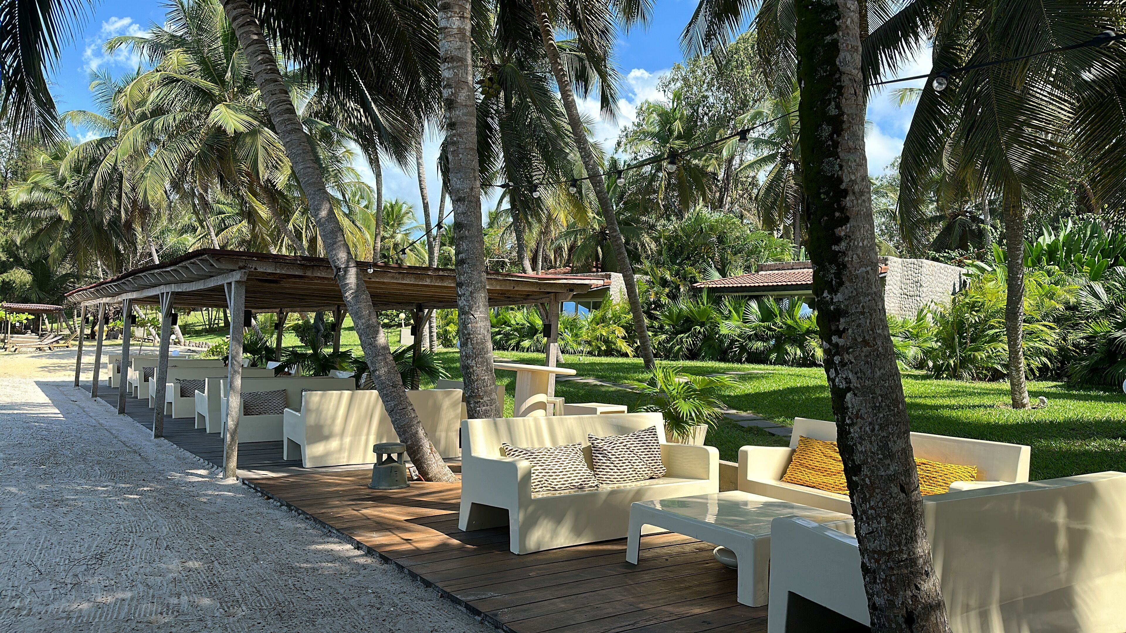 Un resort frente a la playa con mesas al aire libre, palmeras y una zona cubierta.
