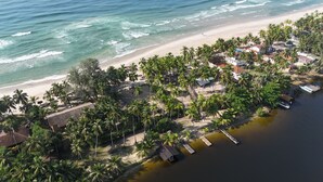 An aerial view of a coastal area with a beach, palm trees, and a dock with boats.