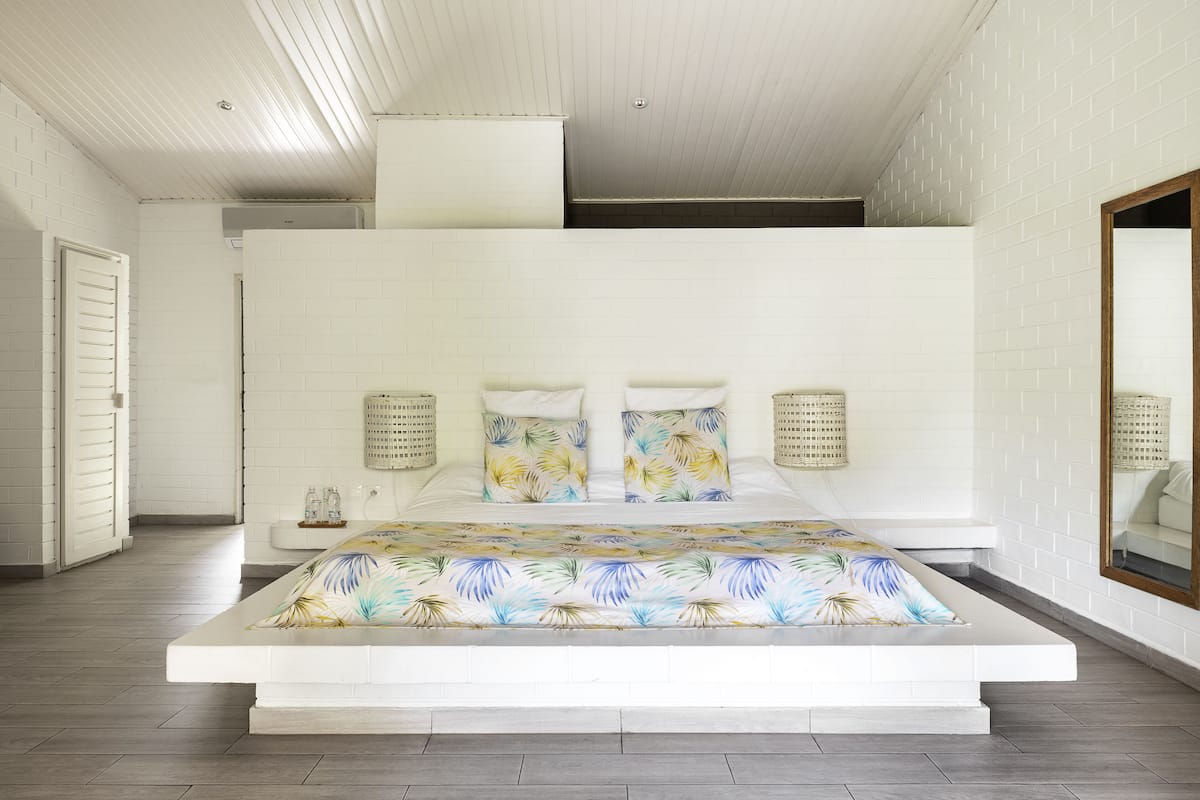 A modern bedroom with a large bed, white walls, and a wooden ceiling.