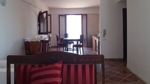 Een ruime woonkamer met een eettafel en stoelen, een grote spiegel en een keuken met een spoelbak en kastjes.