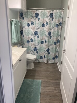 A small bathroom with a toilet, a sink, and a shower curtain with a sea-themed pattern. - Harbor View Cottages-Overlooking Historic  Harbor and Beach (Pass Christian)