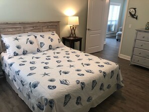 Een slaapkamer met een bed, voorzien van een marine-thema beddeken, een bedlampje en een houten hoofdbord.