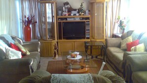 A living room with a TV, wooden cabinets, a glass coffee table, and two sofas. - Fourie Street Guesthouse (Mogalakwena)
