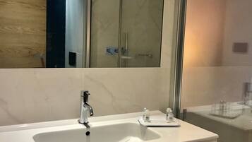 A modern bathroom with a large mirror, a sink, and a glass shower enclosure.