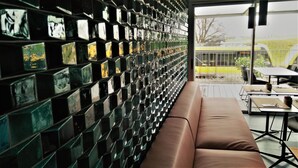 Interior moderno com parede de azulejos refletivos, um banco acolchoado marrom e vista para o exterior através de uma grande janela.