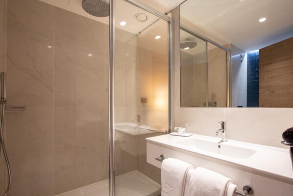 Une salle de bain moderne avec une douche à parois de verre, un meuble-lavabo blanc avec un miroir et un porte-serviettes.