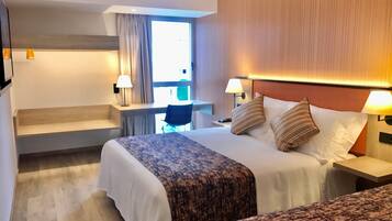Een hotelkamer met twee bedden, een bureau en een raam met gordijnen.