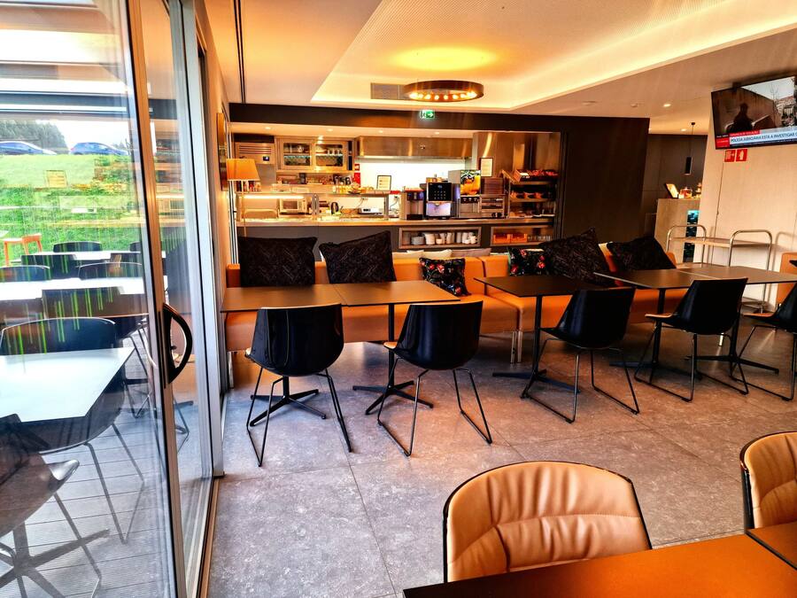 Um saguão de hotel moderno com área de refeições, cozinha e uma grande janela com vista para o exterior.