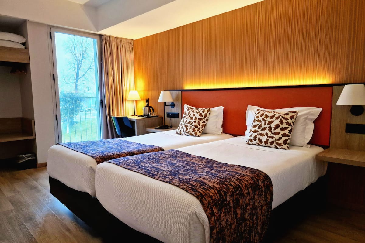 Ett hotellrum med två sängar, ett skrivbord, en stol och utsikt över omgivningarna.
