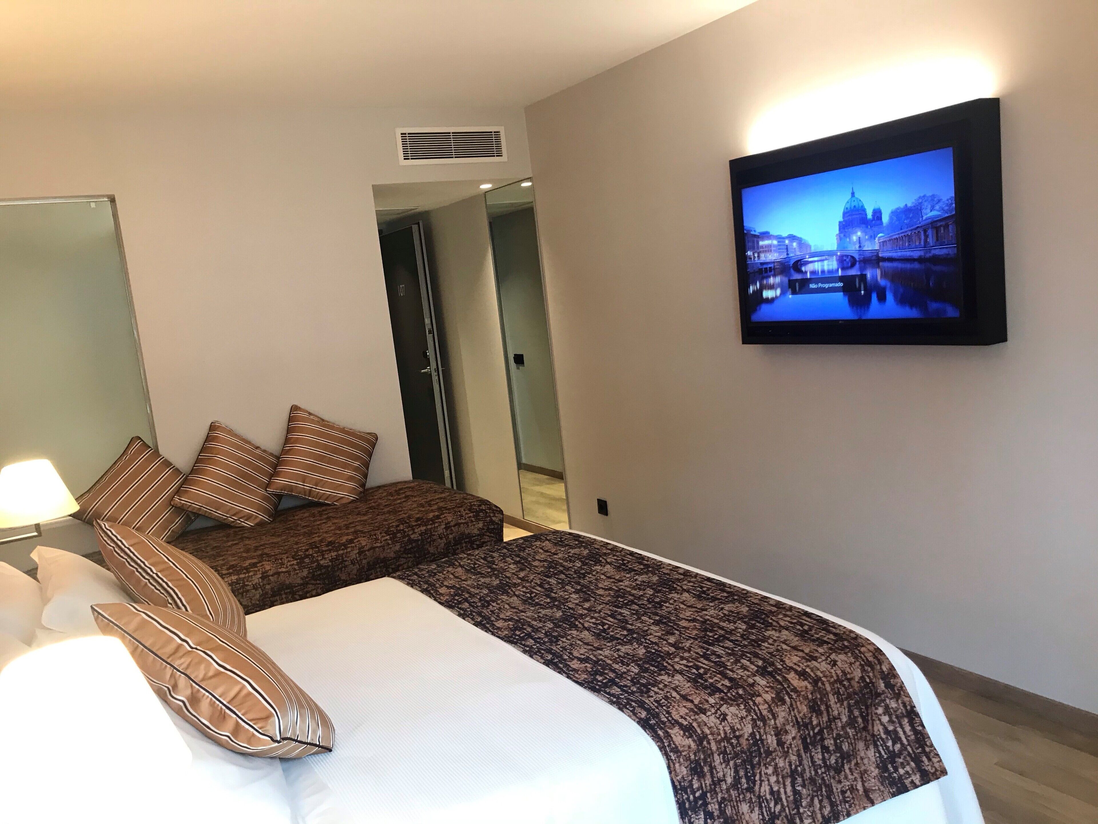 Une chambre d’hôtel avec un lit, deux oreillers, un téléviseur fixé au mur et une porte donnant sur une autre pièce.