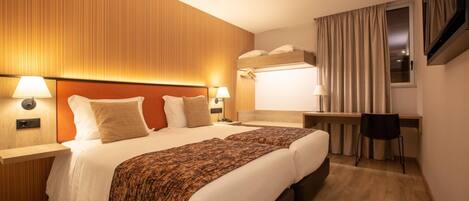 Habitación de hotel con una cama grande, dos mesitas de noche con lámparas, un escritorio con una silla y un televisor montado en la pared.